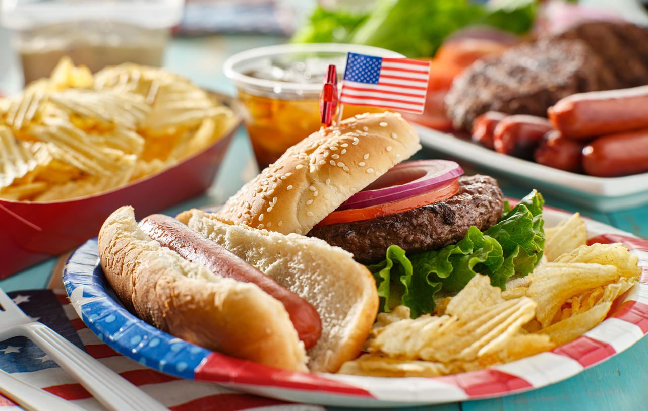 Patriotic American BBQ spread featuring a sesame seed burger, grilled hotdog, and crispy fries with flag decoration, ideal for foodservice and wholesale catering.