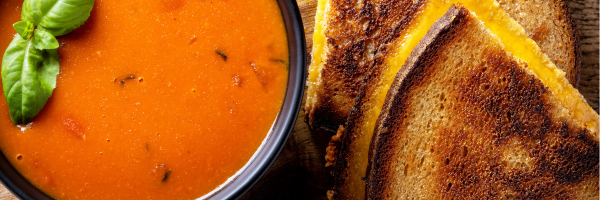 Creamy tomato soup in a bowl paired with golden grilled cheese sandwich, ideal for foodservice and commercial food suppliers.